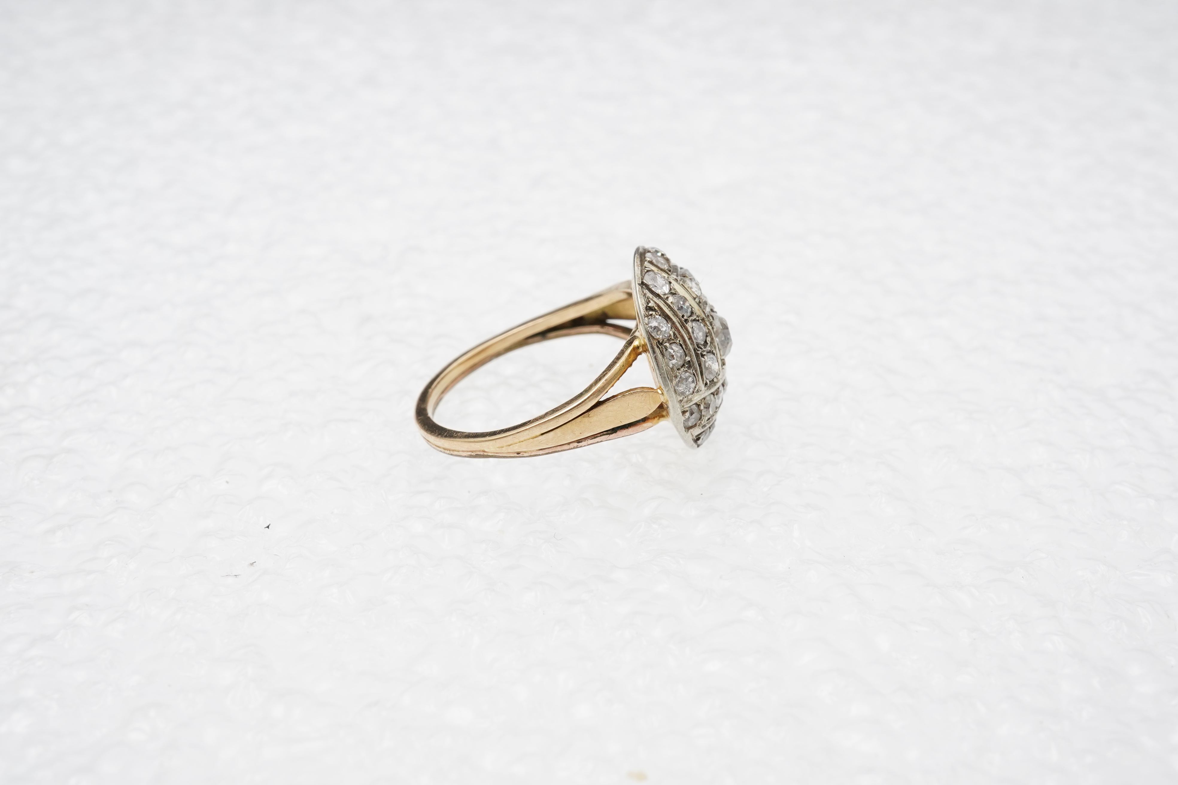 A diamond ring, centring on a circular motif of bombé design, set with geometric arrangements of cushion-shaped, single- and circular-cut diamonds totalling approximately 0.90 carats, to a gold band, size M1/2, indistinc